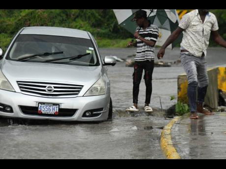 A motorist got stuck at a section of Chesterfield Avenue in Seaview Gardens, St Andrew, as the rain conditions worsened yesterday. Both the driver and his son attempted to get the vehicle out of a large hole.