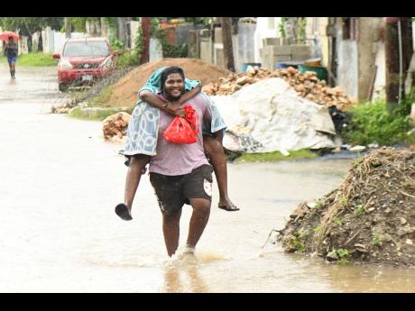 Residents of Riverside Drive in New Haven, St Andrew, make their way through floodwaters caused by the heavy downpour during the passage of Tropical Storm Rafael on Tuesday.