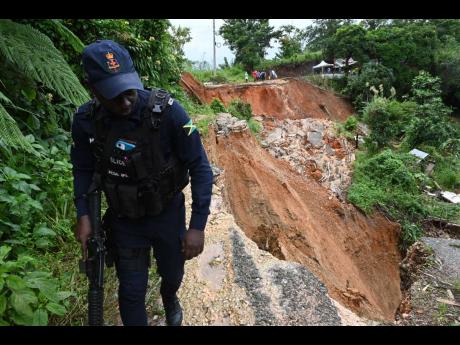 A policeman walks along the edge of a section of the McGlashen main road that was cut away in recent days as a result of heavy rainfall in 
St Andrew West Rural. 