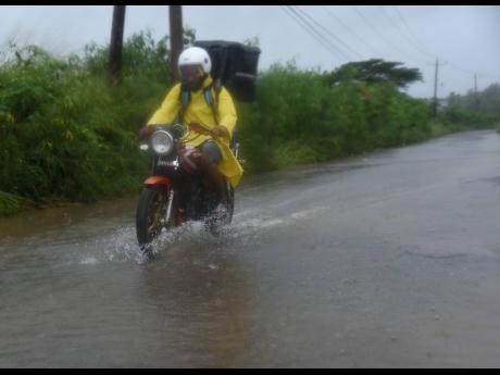 A delivery man rides through a flooded section of St John’s Road in 
St Catherine, during rains caused by the passage of Tropical Storm Rafael on Tuesday.