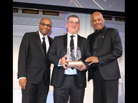 Credit: Derrick Scott Honoree William Mahfood, WISYNCO group chairman (centre), displays his Chancellor’s Award for Excellence in Global Business Leadership and Philanthropy memorabilia. Also in photo are (from left) Dr Ronald Chase, AFUWI board member, and Professor Sir Hil