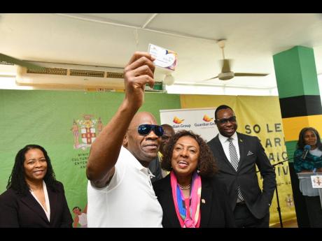 Credit: JIS News Minister of Culture, Gender, Entertainment and Sport, Olivia Grange (second right), with singer George Nooks (second left), who proudly shows his health card received during Tuesday’s (August 19) contract signing at the Ministry's Office in St Andrew bet