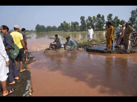 Credit: AP Villagers help a milkman crossing the flooded portion of a road damaged by floods after torrential rains on the outskirts of Sodhra town, in Wazirabad district, Pakistan.