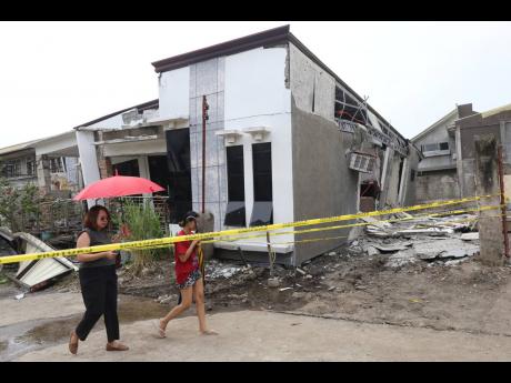 Credit: Manman Dejeto Two women walk past a damaged house after a strong earthquake in Davao City, southern Philippines on Friday October 10, 2025. (AP Photo/Manman Dejeto)