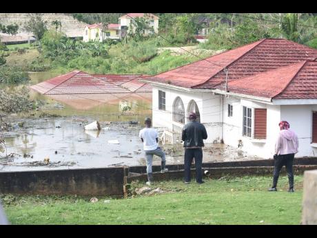Onlookers view houses and motor vehicles that were left submerged on Gibson Close in Mandeville, Manchester, after the passage of Hurricane Melissa.