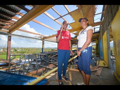Credit: JIS News Principal of St Elizabeth Technical High School (STETHS), Keith Wellington, takes calls from persons offering well wishes and support, while the institution’s Acting Vice Principal Patrine Daley-Chambers, looks on the damage to the grade 11 block. STET