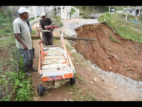 Credit: Ian Allen/Photographer A man pushes a cart across a slither of roadway left in a section of Lorrimers, Trelawny, after a major breakway was triggered by Hurricane Melissa.