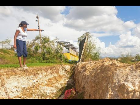 Credit: JIS News St Elizabeth Technical High School (STETHS) Acting Vice Principal, Patrine Daley-Chambers, points to the section of the perimeter wall that broke away during the passage of Hurricane Melissa.