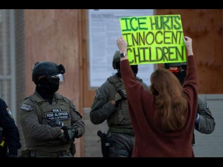 A protester holds a sign as law enforcement officers stand outside a United States Immigration and Customs Enforcement (ICE) facility in Portland, Oregon, on Tuesday, October 21, 2025. (AP Photo/Jenny Kane, File)