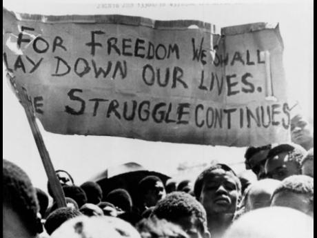 A banner is held aloft above black students in Johannesburg, South Africa, in the township of Soweto where they rallied after the funeral of a 16-year-old black student who died in jail on October 18, 1976. 